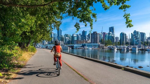 On a sunny summer day, a woman enjoys a leisurely bike ride along the seawall in stanley park, with
