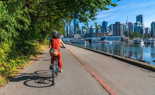 Tourist wearing helmet and orange jumpsuit is riding bicycle on seawall in stanley park with