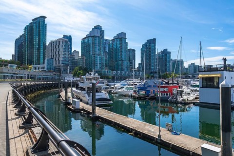 Modern buildings rise above a marina filled with yachts and houseboats, creating a picturesque
