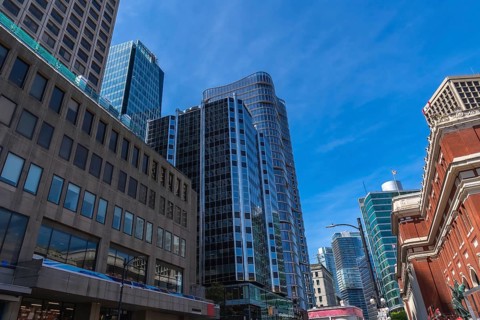 Modern glass skyscrapers and historical brick buildings stand tall against a vibrant blue sky,
