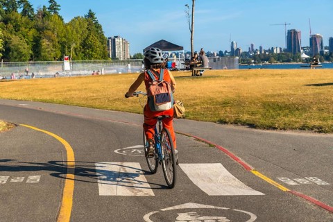 Tourist enjoying cycling in kitsilano beach park with english bay and the city of vancouver skyline