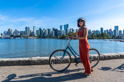 Young woman wearing a helmet stands next to her bicycle, enjoying a scenic waterfront view of