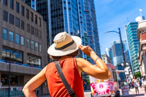 Young woman tourist holding her straw hat is admiring the skyline of vancouver downtown in british