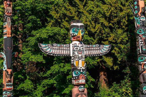 Colorful totem poles rise against a backdrop of lush green trees, reflecting the rich history and