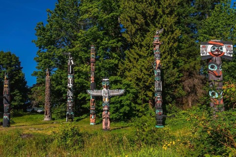 Totem poles standing tall against a backdrop of lush trees and blue sky, showcasing the rich