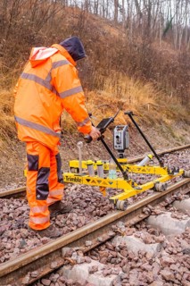 Construction worker with measuring device device works on yellow equipment on rails in winter,
