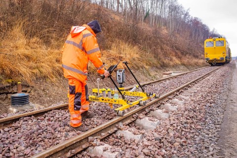A worker operates a yellow device on the railroad tracks in an autumn landscape, stuffing machine