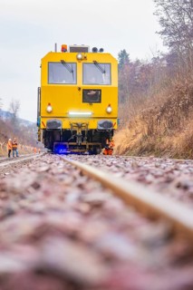 Yellow vehicle on gravel with construction workers in the forest, tamping machine on Hermann,