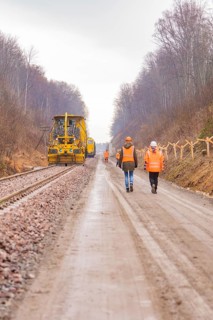 Construction worker on a rail line in the forest, accompanied by a yellow machine, tamping machine