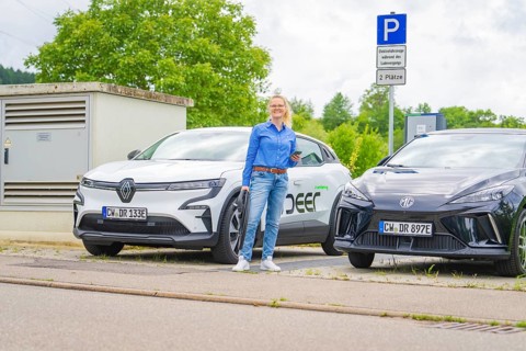 Two electric cars park side by side at a charging station, surrounded by green countryside, Deer