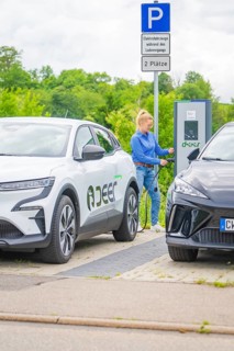 Woman connects Renault electric car to charging station in a municipal parking lot, Deer