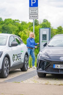 Woman refuels electric car at a charging station between two parked vehicles, Deer E-Carsharing,