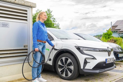 Woman wearing a blue shirt charges a white electric car at a charging station, Deer E-Carsharing,