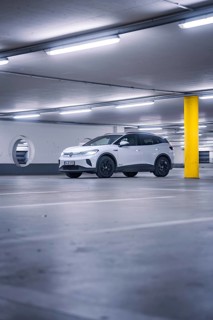 White car in empty underground garage with yellow pillar and neon light atmosphere, deer e-car