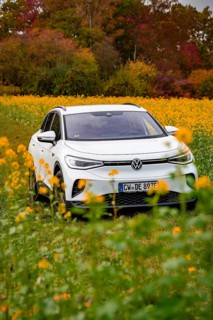 A white SUV drives through a blooming field surrounded by autumn trees, Deer E-Carsharing, VW ID4,