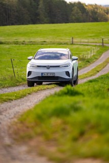 White car driving on a dirt road through green meadow landscape in daylight, Deer E-Carsharing, VW