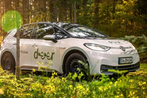 A car stands between trees in the forest with a pleasant light show, Deer E-Carsharing, VW ID3,