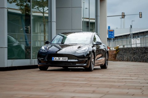 Black car in front of a modern building with wet road and cloudy sky, Deer E-Carsharing, Tesla