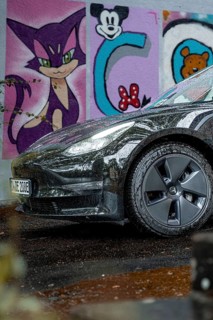 Close-up view of a black car in front of colorful graffiti art on a wet road, Deer e-car sharing,