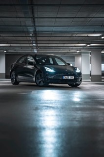 Black car in a modernly lit parking garage at night with reflective floor surfaces, Deer e-car