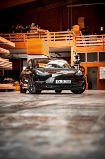 Black car in an industrial-looking workshop with wooden details, parked on concrete floor, deer