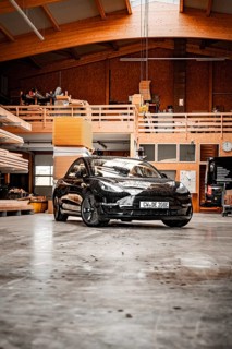 Black car parked in a wood-panelled workshop with modern architectural design, Deer e-car sharing,