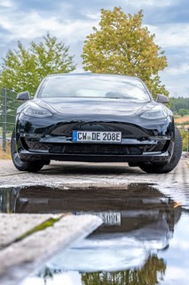 Front view of a black car with puddle reflection and tree in the background, Deer E-Carsharing,