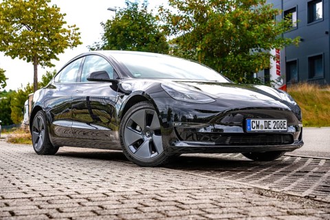 Black car on an urban road in front of modern buildings and trees, Deer E-Carsharing, Tesla Model