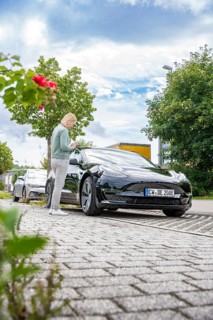 Person standing next to black car on paved road under blue sky with clouds, Deer E-Carsharing,