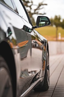 Side view of a reflecting black car, in focus a side mirror, Deer E-Carsharing, Tesla Model 3,