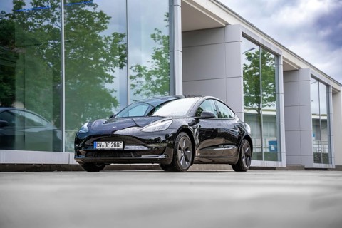 Black Tesla in front of a glass building with trees in the background, Deer e-Carsharing, Tesla