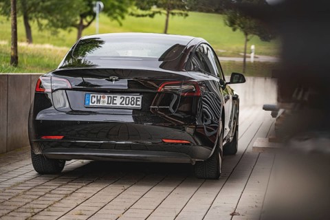 Black car from behind on a road with green landscape in the background, Deer e-Carsharing, Tesla