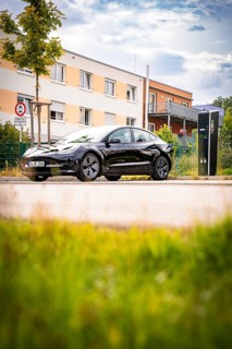 Black car at a charging station in front of a modern building backdrop under a blue sky, Deer