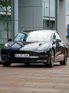 Black car with rain droplets on paint in front of glass buildings, Deer E-Carsharing, Tesla Model