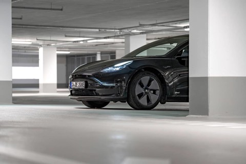 Black Tesla partially visible in a brightly lit parking garage, Deer e-Carsharing, Tesla Model 3,