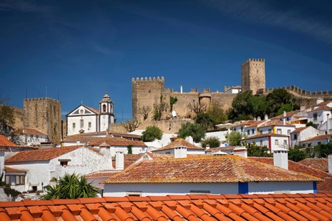 Obidos features a stunning medieval castle rising above white houses and terracotta rooftops,