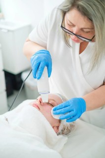 A pro esthetician cosmetologist uses a metal spatula for ultrasonic facial cleansing to exfoliate