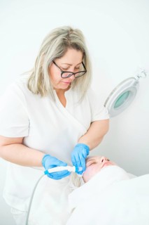 Cosmetologist in blue gloves delivers a hydrafacial cleansing treatment to a client, using blue