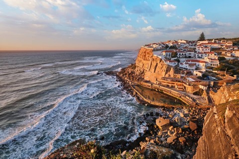 The picturesque village of Azenhas do Mar is illuminated during sunset, resting on cliffs above the