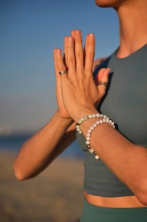 A woman practices yoga by holding hands in Namaskar Mudra at the beach as the sun sets in the
