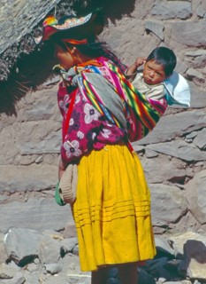 Young woman wearing traditional clothing carries her small child in a traditional way on Isla