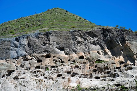 A steep mountain with numerous caves under a clear blue sky, cave town, cave monastery, Vardzia,