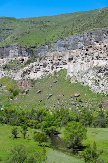 Rocks with engraved caves surrounded by green grass and trees, cave town, cave monastery, Kura