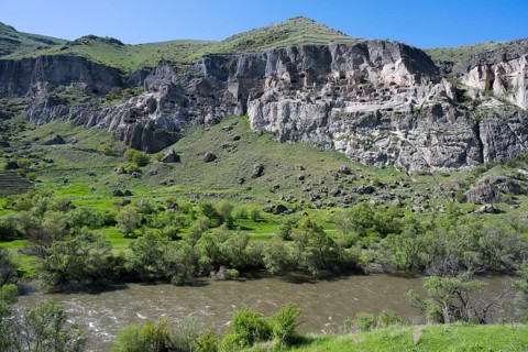 Rocky cliffs and flowing river in a green setting. Picturesque scenery, Kura river, cave monastery,