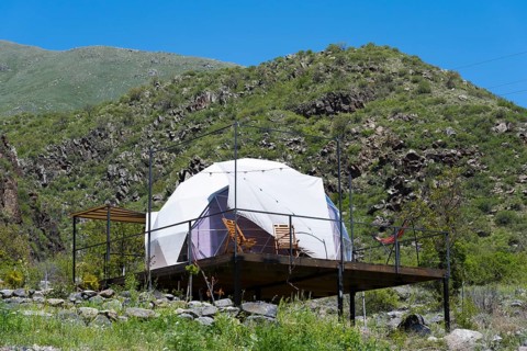 Dome tent on a wooden terrace in green mountain landscape under blue sky, Vardzia Glamping,