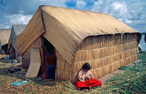 Little girl sitting in front of a reed hut on a floating Uro island in Lake Titcaca, Peru, South