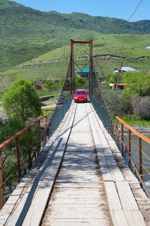 A car drives across a wooden suspension bridge in green surroundings, Kura River near Nijgori,