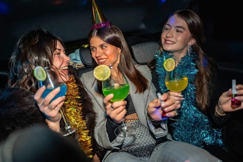 Young women celebrating new year's eve on their way to a party, holding colorful cocktails and