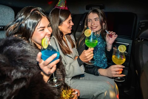 Young women are celebrating a new year's eve party inside a car, holding colorful cocktails and