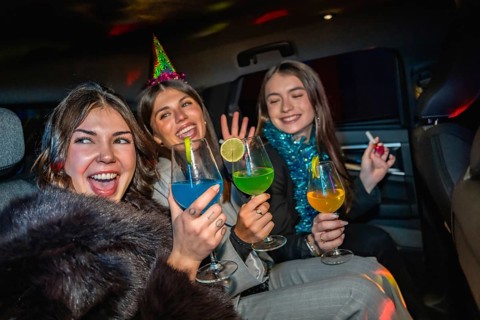 Young women friends celebrating new year's eve, cheering with colorful cocktails while traveling in